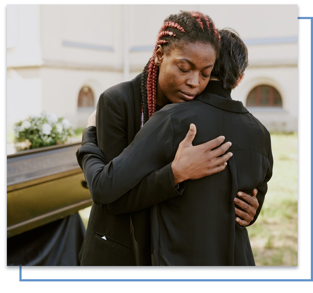 Two people embrace at an outdoor funeral service, conveying grief and support.