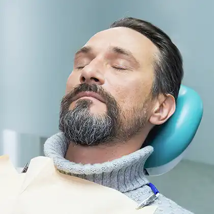 man who received dental sedation laying back in dentist chair with eyes closed