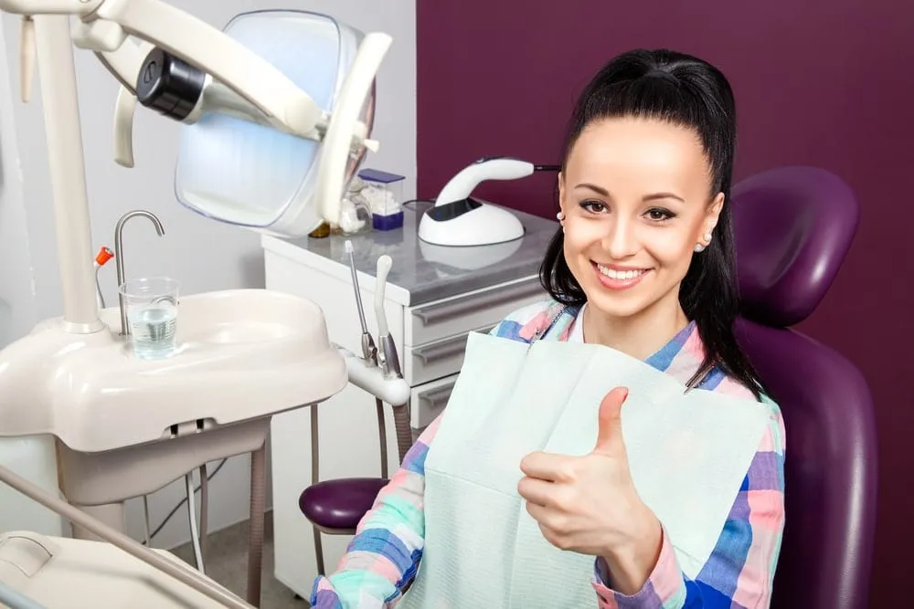 Woman giving a thumbs-up while seated in a dental chair